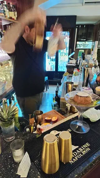 Bartender vigorously shaking a cocktail behind the counter, with a coconut in an oversized glass nearby