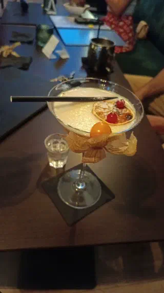 Signature cocktail garnished with physalis and a dried orange slice on a wooden bar table