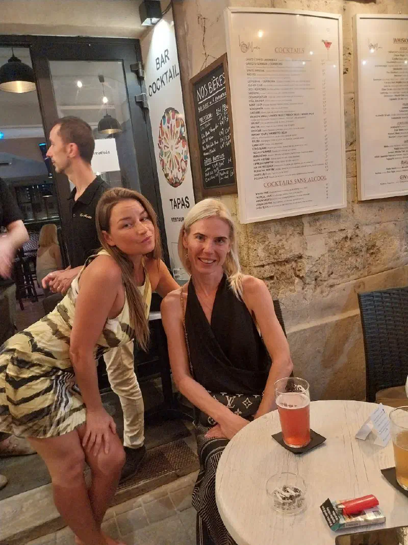 Two guests of the evening at a table, smiling, with drinks and cocktail menus on the wall behind