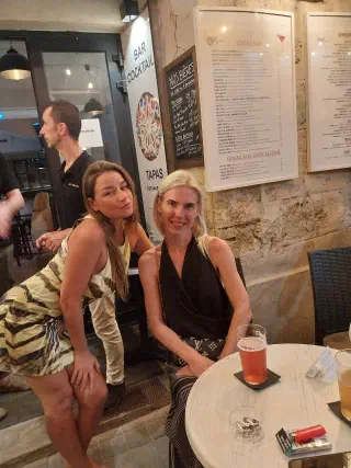 Two guests of the evening at a table, smiling, with drinks and cocktail menus on the wall behind