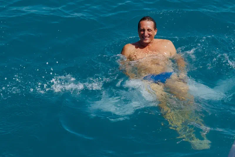 A smiling man swims in the turquoise sea amid splashes