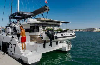 Catamaran at the marina dock: the skipper readies the boat, a dinghy hoisted at the stern