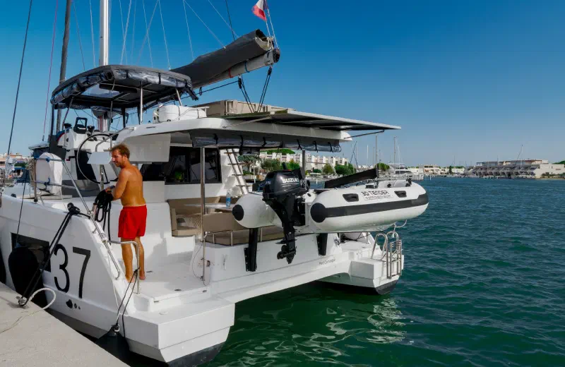 Catamaran at the marina dock: the skipper readies the boat, a dinghy hoisted at the stern