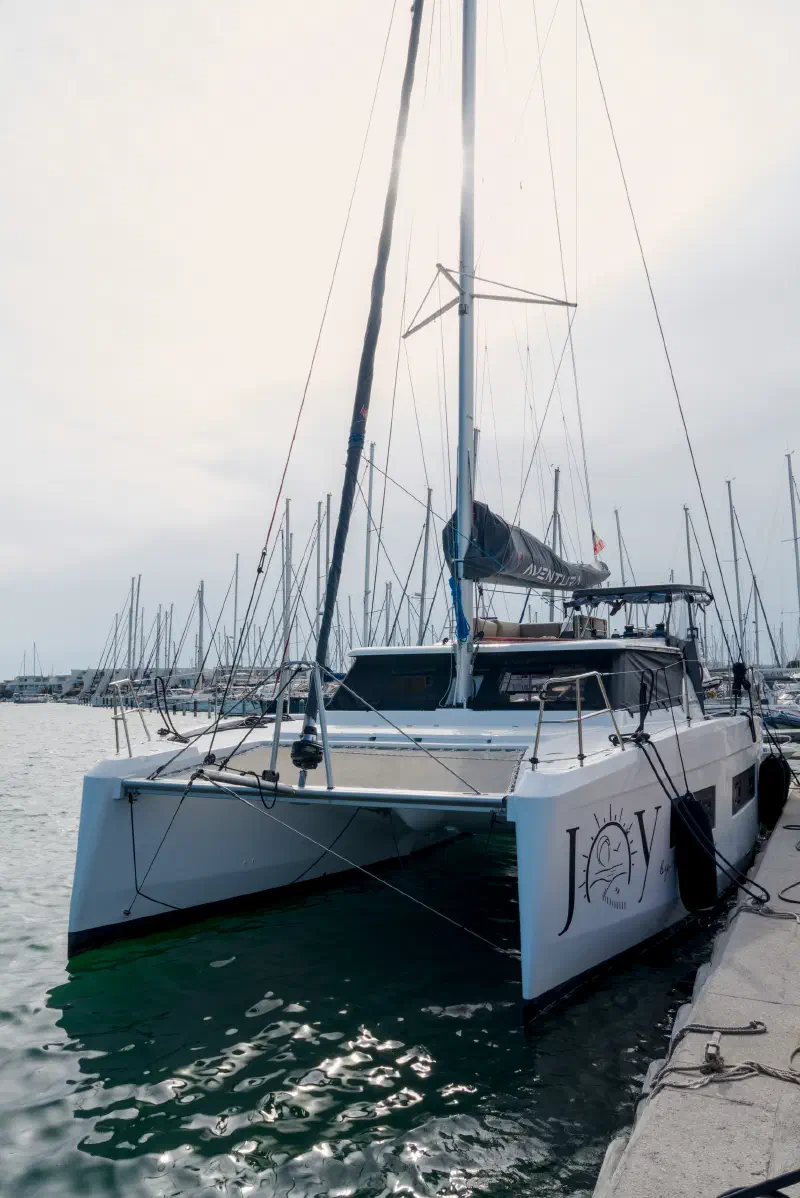 White catamaran with a bow trampoline at a Le Grau-du-Roi marina pontoon in morning haze
