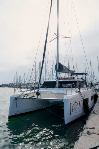 White catamaran with a bow trampoline at a Le Grau-du-Roi marina pontoon in morning haze