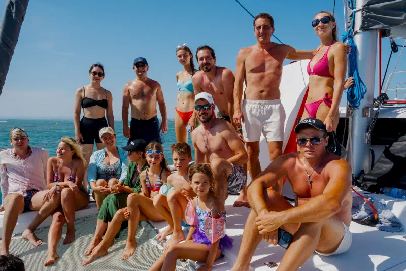 Group photo on the catamaran's bow: adults and children against the sea and sky