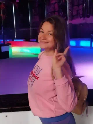 A young woman posing by the boards of the ice rink, the arena glowing with multicoloured neon