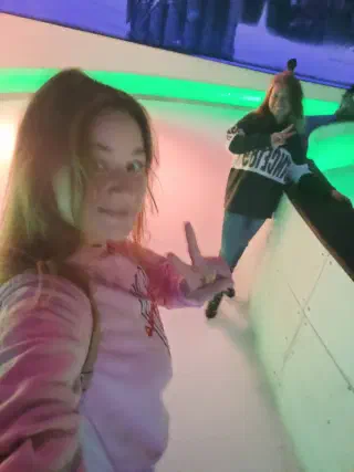 Rink selfie: both skaters flashing peace signs, the ice lit up with green neon