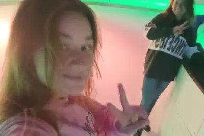 Rink selfie: both skaters flashing peace signs, the ice lit up with green neon
