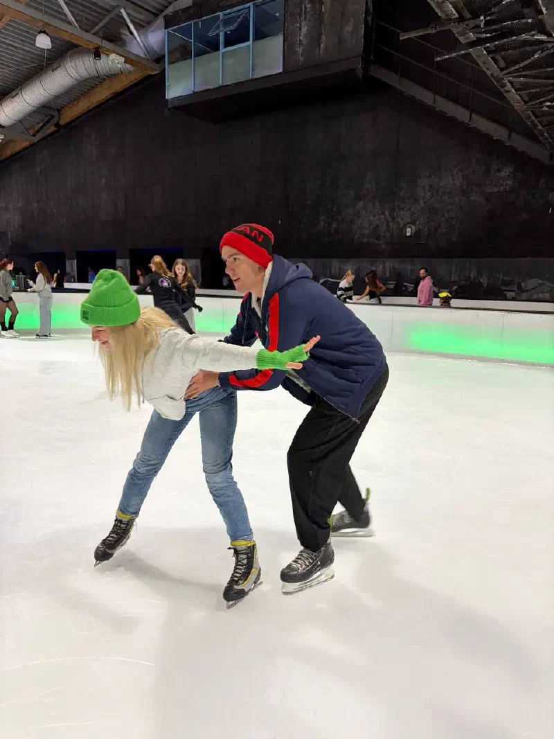 One skater holds another by the hands, helping them stay up on the ice