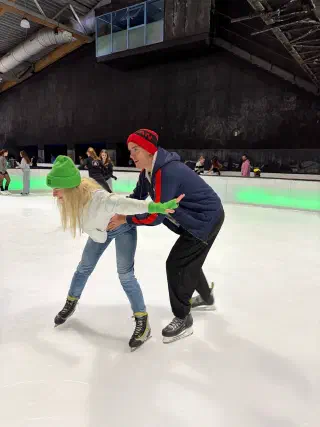 One skater holds another by the hands, helping them stay up on the ice