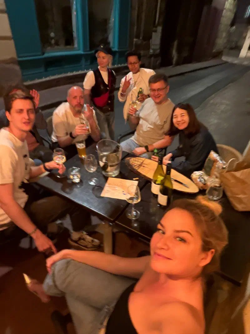 The group keeps the evening going at an outdoor table: beer, wine and baguettes at night