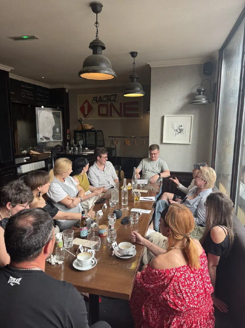 Players around a long table with numbered cards — the afternoon Mafia game in the pub room