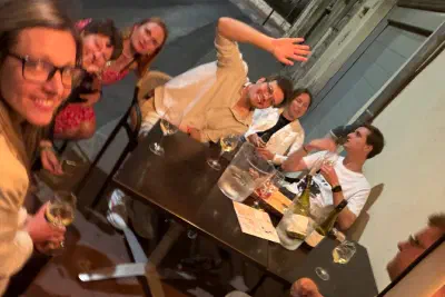 Group selfie at a street table late in the evening, with wine, a water jug and big smiles