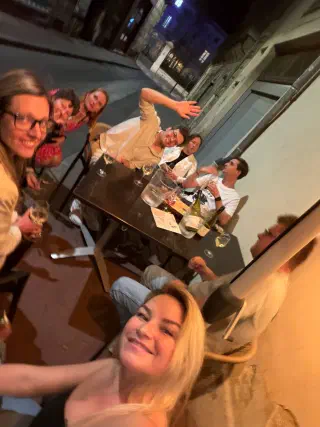 Group selfie at a street table late in the evening, with wine, a water jug and big smiles
