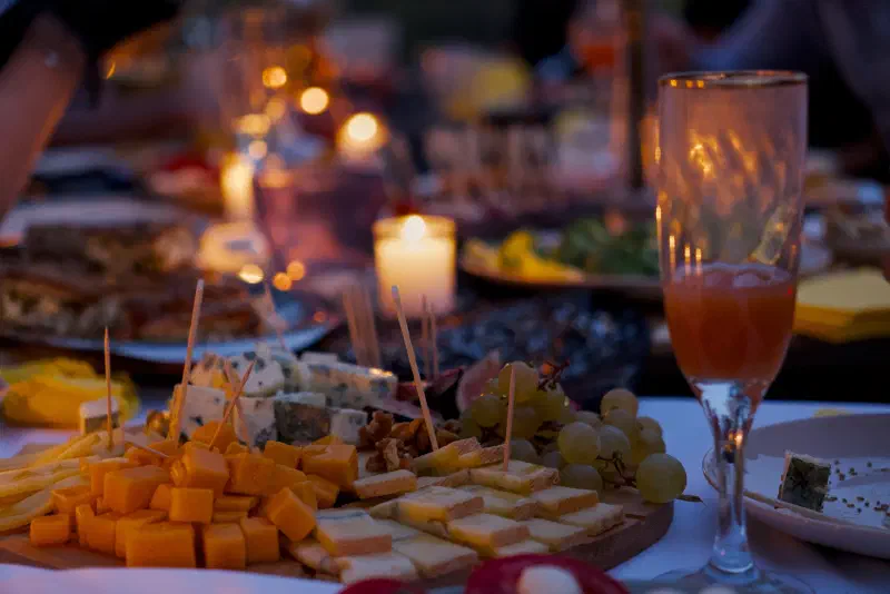 A cheese board with grapes and walnuts on the table by candlelight at dusk, blurred lights and guests behind