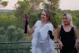 Two guests in 1920s outfits at the terrace railing: a silver fringed dress, a white feather boa, long gloves and pearls