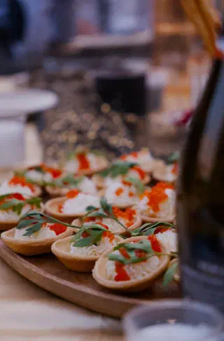 Tartlets with red caviar and herbs on a wooden board, the table's glitter runner behind