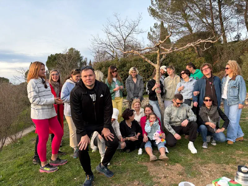 Evening group photo around a young tree on a lawn; a girl with a plush unicorn sits in front