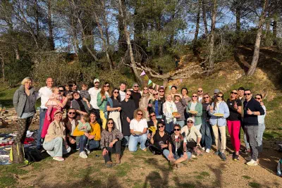 A big group posing with plates of pancakes under pine trees in a sunny park, with bunting strung on a tree