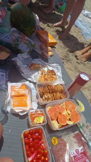 Picnic spread on a beach blanket: a watermelon, home-baked pies in foil, fruit and snacks in containers