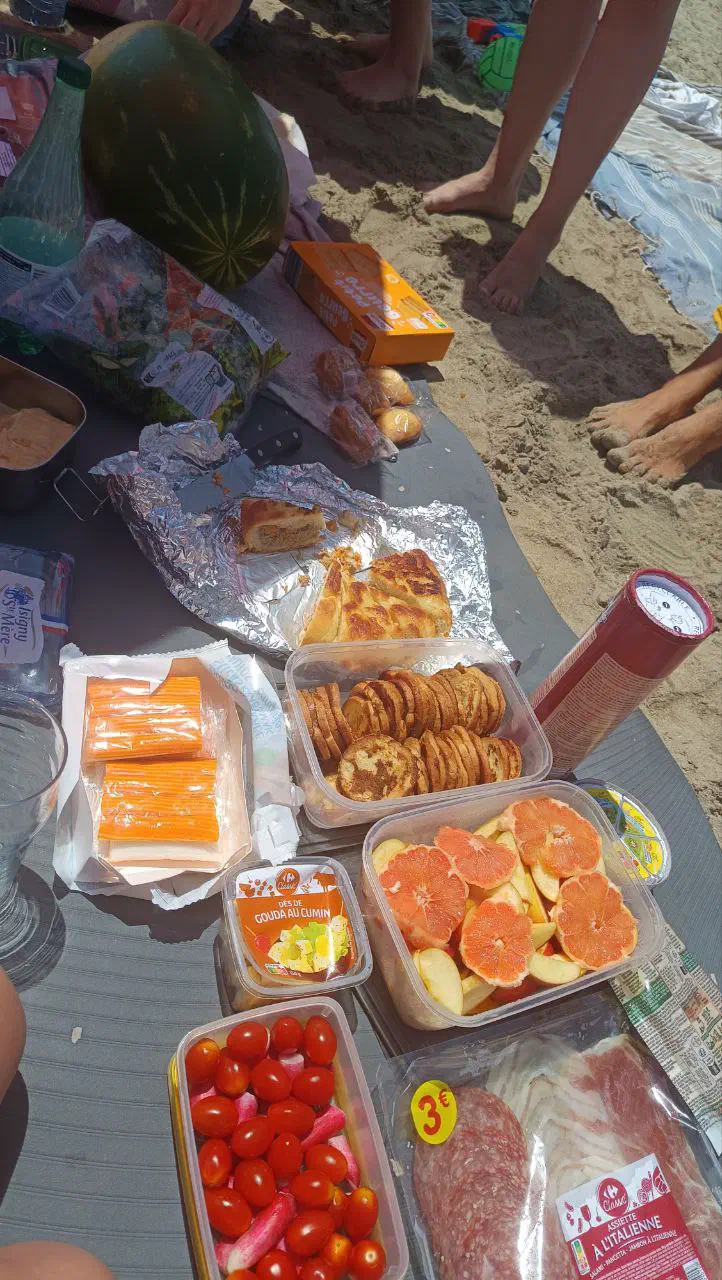 Picnic spread on a beach blanket: a watermelon, home-baked pies in foil, fruit and snacks in containers