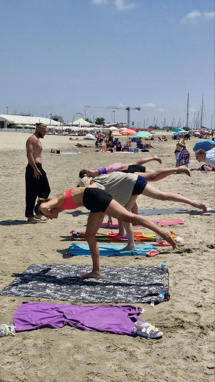 Yoga practice on mats — one-leg balance poses; yacht masts and a Ferris wheel in the distance