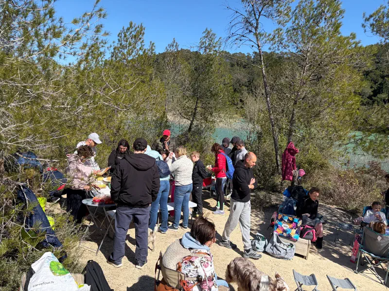 Picnic at Lac de Cécélès: people around folding tables with food, turquoise water behind the pines