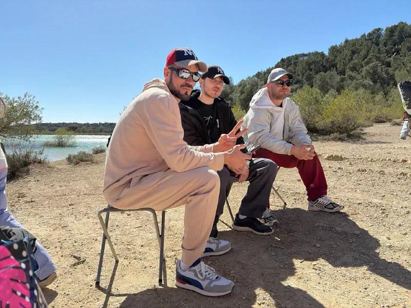 Three hikers in caps relaxing on folding stools by the lakeshore