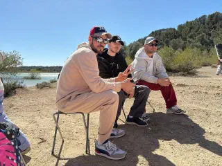 Three hikers in caps relaxing on folding stools by the lakeshore