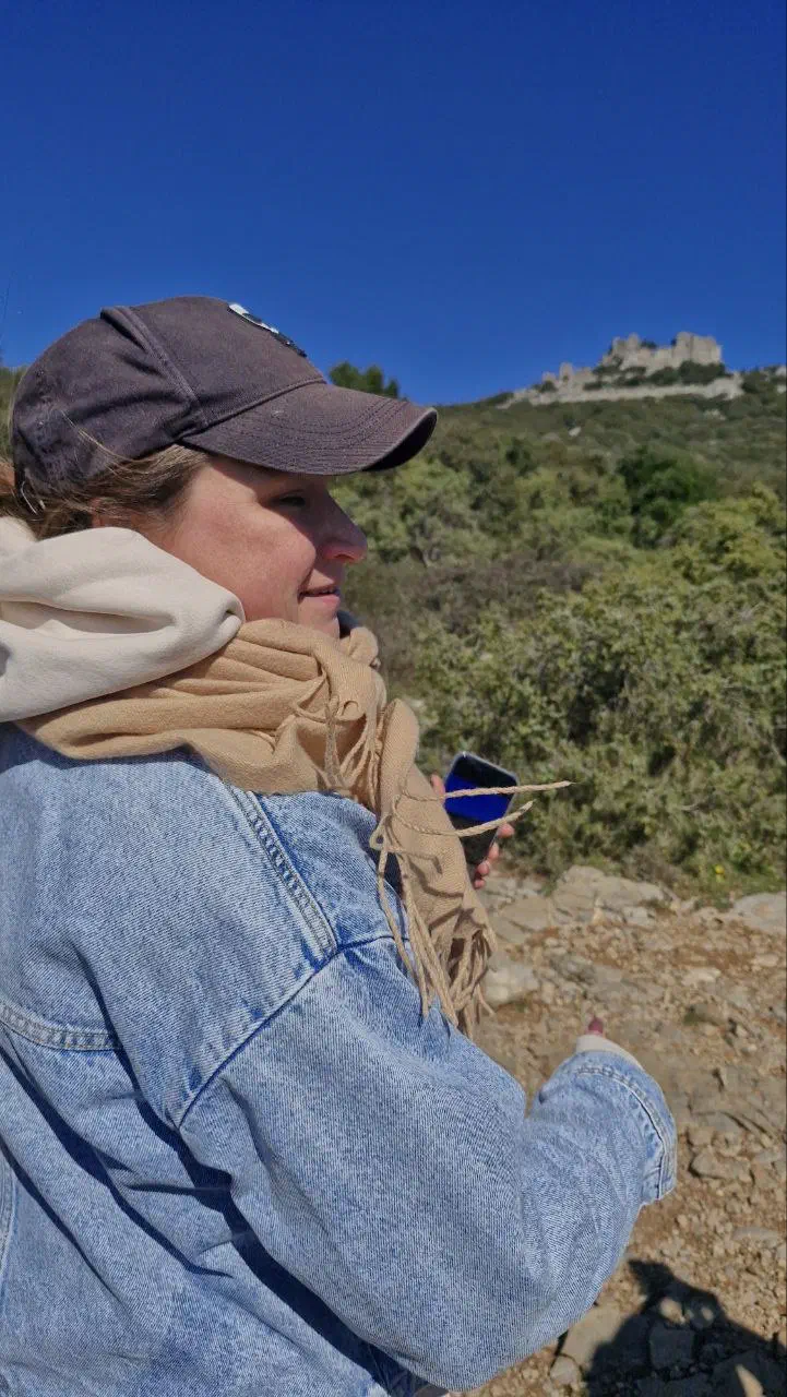 Hiker in a cap and scarf on the trail, castle ruins on the hill in the distance