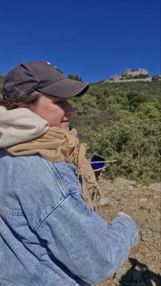 Hiker in a cap and scarf on the trail, castle ruins on the hill in the distance
