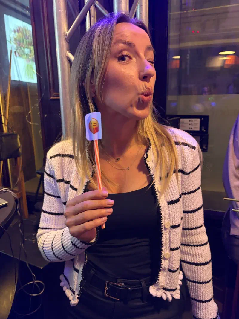 A guest in a striped cardigan blowing a kiss while holding an emoji photo prop on a straw