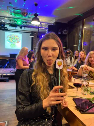 A guest goofing around with an emoji stick prop; behind her the bar stage, a disco ball and tulips on the screen