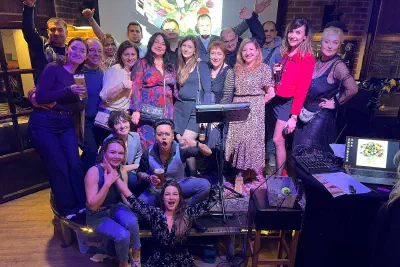 Party group shot in a bar: a dressed-up crowd by the stage with a bouquet of tulips on the screen behind them
