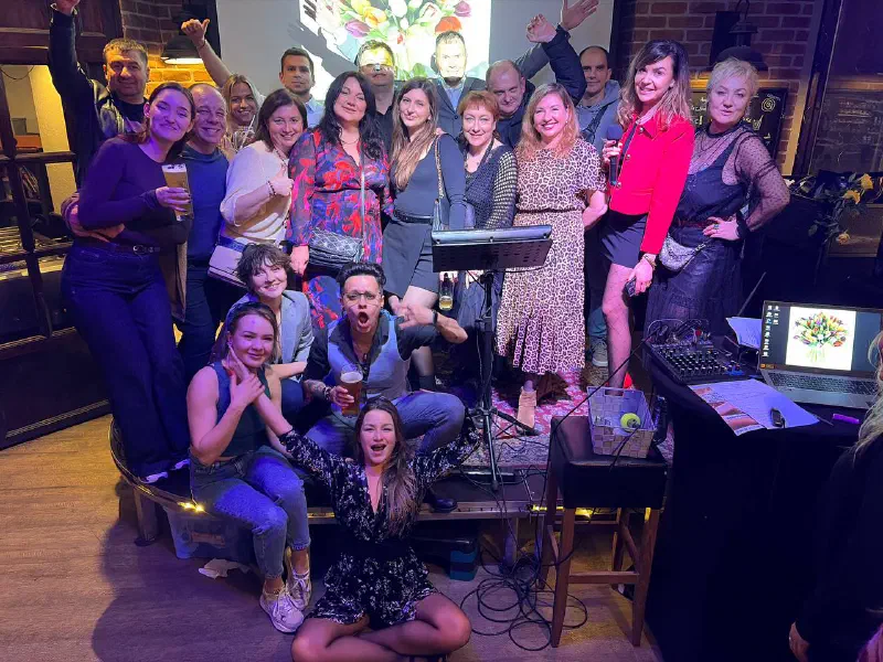 Party group shot in a bar: a dressed-up crowd by the stage with a bouquet of tulips on the screen behind them