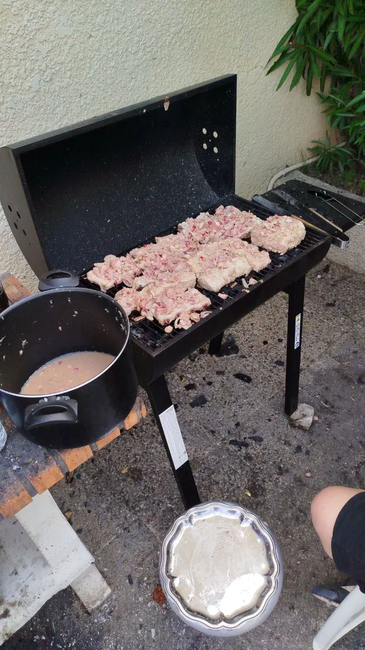 Marinated meat laid out on a barbecue grill next to a pot of marinade