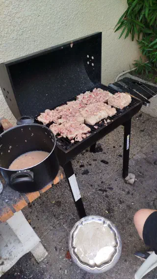 Marinated meat laid out on a barbecue grill next to a pot of marinade