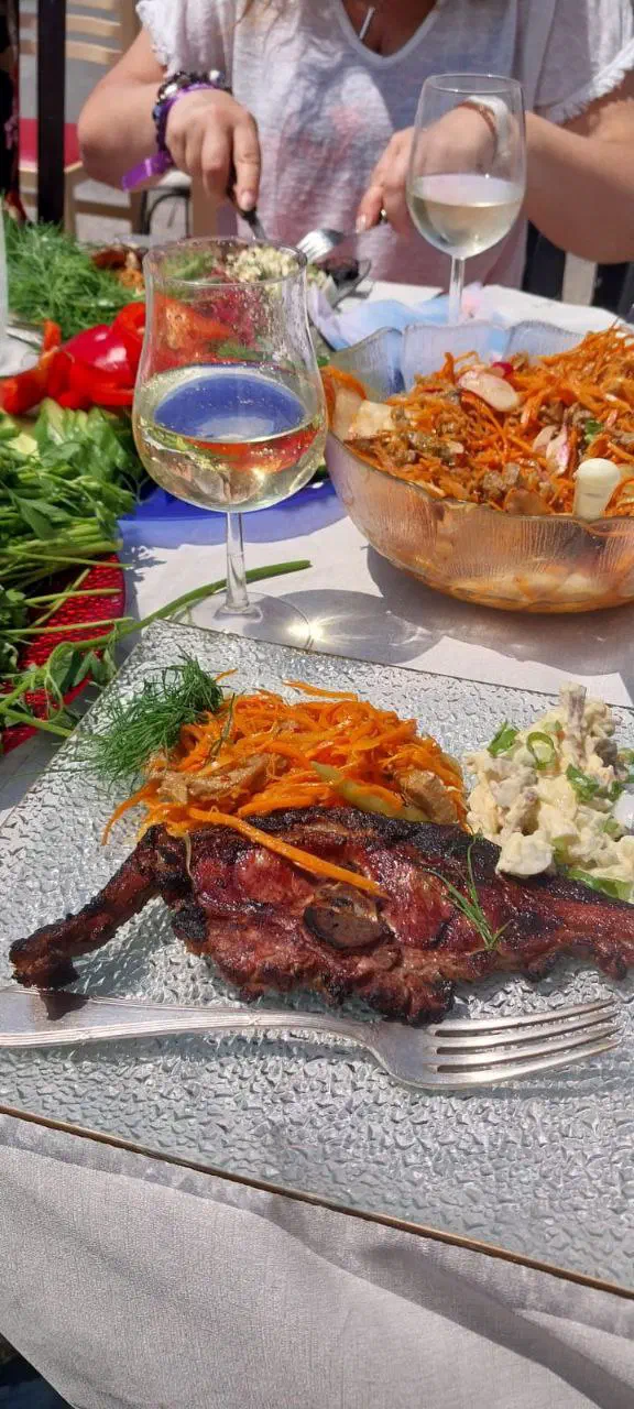 Plate of grilled shashlik with Korean-style carrot and salads, a glass of white wine beside