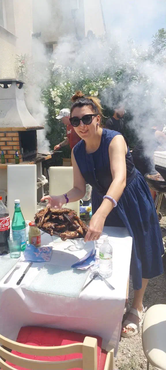 Woman placing a large platter of grilled shashlik on the table amid barbecue smoke