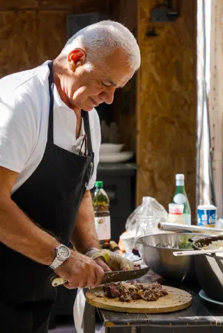 The plov master in a black apron cuts boiled lamb on a wooden board