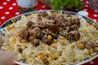 Uzbek plov with lamb, carrots and chickpeas on a large platter, red polka-dot tablecloth