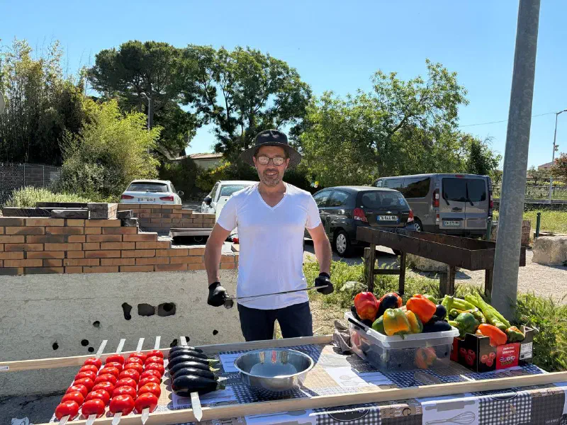 Grill master in a hat prepping vegetables: skewered tomatoes and eggplants, crates of peppers