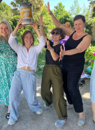 Four women strike a playful pose lifting a small keg overhead