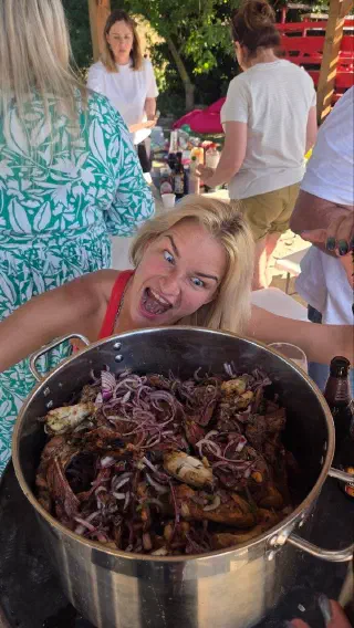Huge pot of grilled meat with red onion and a delighted guest posing behind it