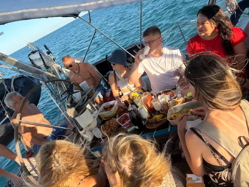 The group around a table of snacks and drinks in the yacht's cockpit, open sea all around