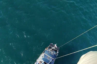 View down from the mast onto the deck of a sailing yacht at sea, with the group gathered on deck