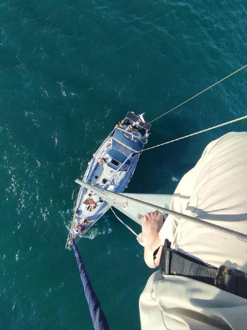 View down from the mast onto the deck of a sailing yacht at sea, with the group gathered on deck